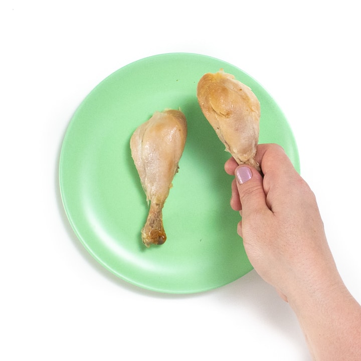 Hand showing how to have baby hold a piece of chicken.