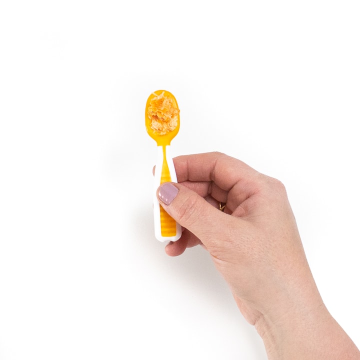 Hand holding a baby spoon with mashed chicken and carrots on it.