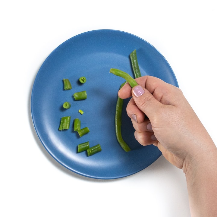 Hand holding a green bean over a plate of green beans.