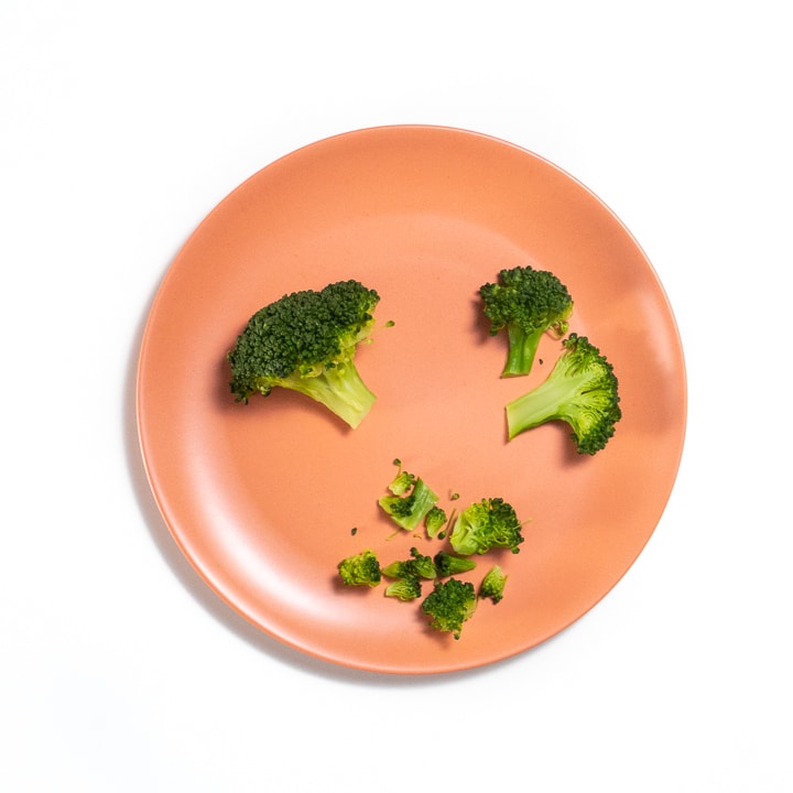 Orange baby plate with broccoli cut and chopped on it.