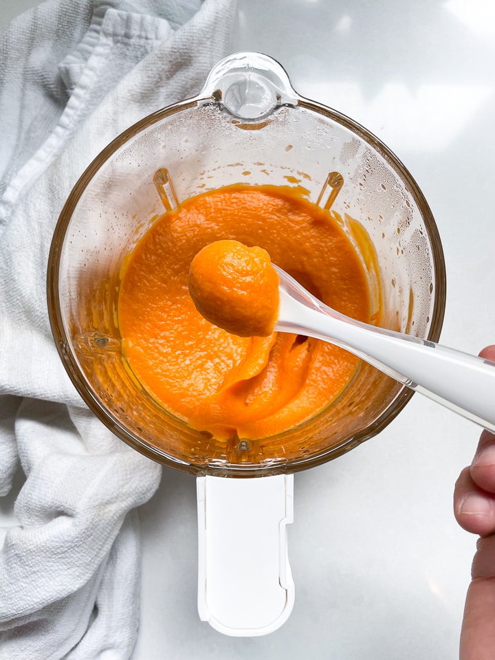 Glass blending jar with pureed sweet potato with spoon holding some of the puree.