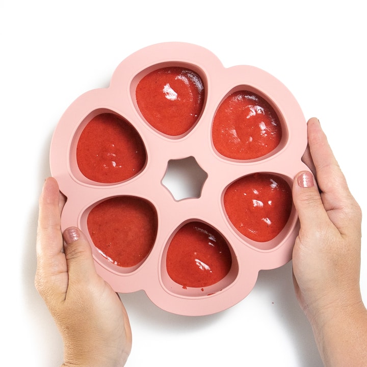 Hands holding a pink freezer tray with pink strawberry puree inside.