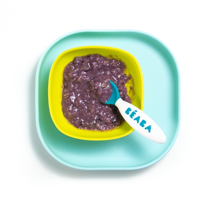 Teal plate with green bowl with purple blueberry oatmeal inside.