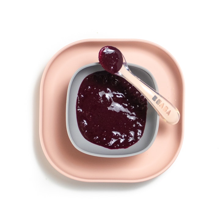 Pink baby plate with gray bowl full of blueberry puree.