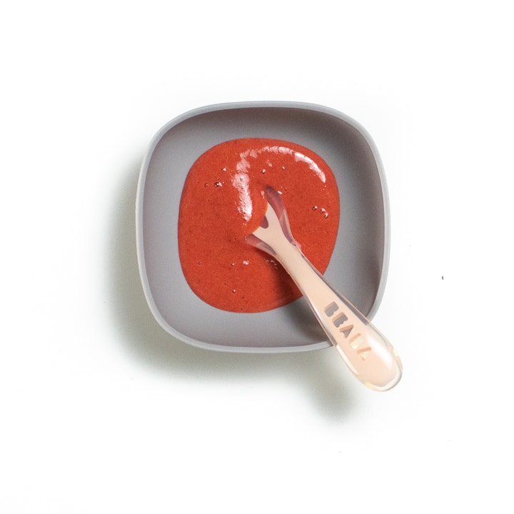 Pink spoon resting in a gray bowl filled with strawberry puree.