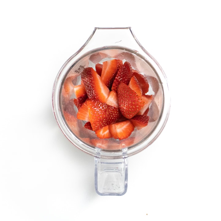 Small blender with fresh chopped strawberries inside.