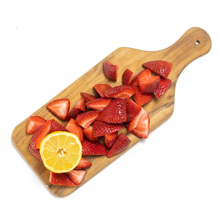 Cutting board with strawberries and a lemon.