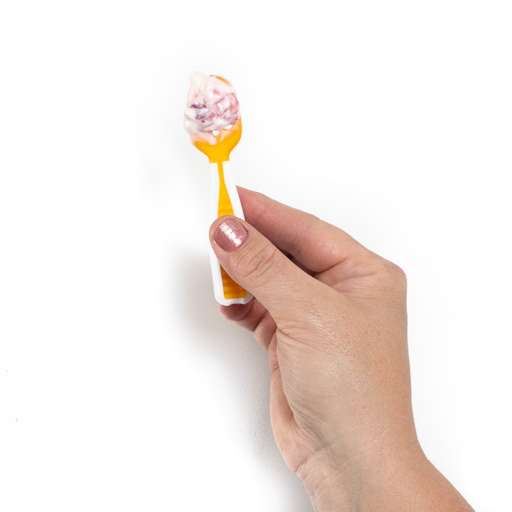 Hand holding a baby spoon that is loaded with yogurt and strawberries.