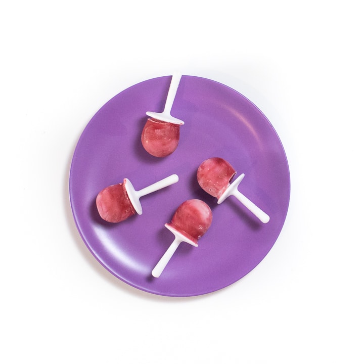 Purple baby plate with pink and white popsicles on it.