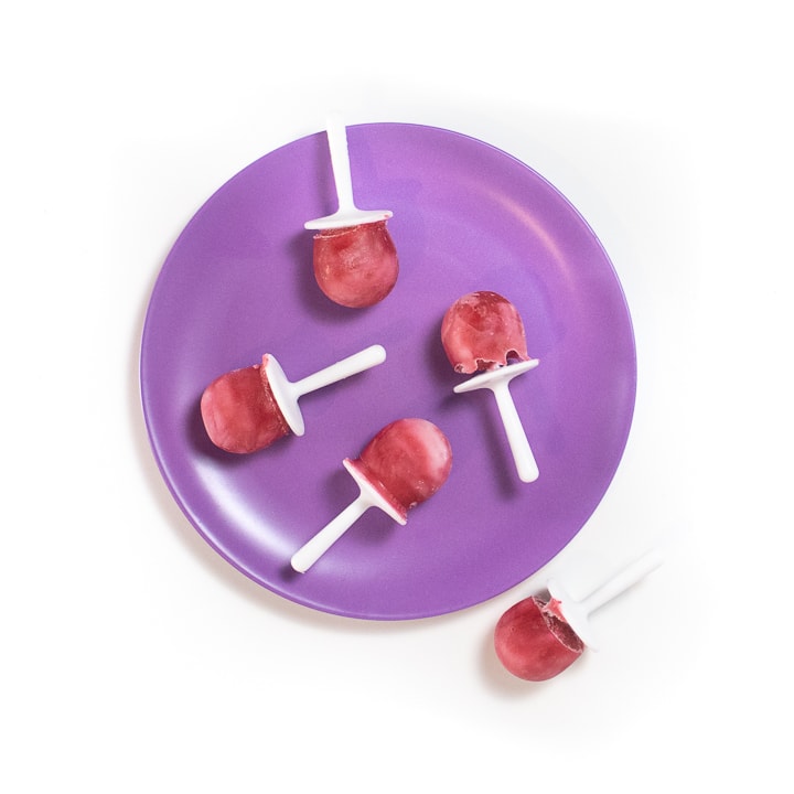 Purple baby plate with pink and white popsicles on it.