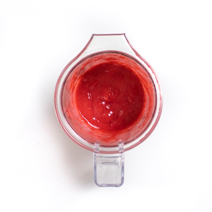 Small clear blender with raspberry puree inside.
