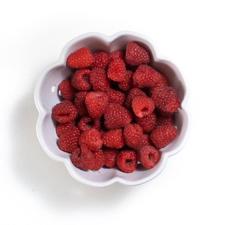 White bowl with scalloped edges with fresh raspberries in it. 