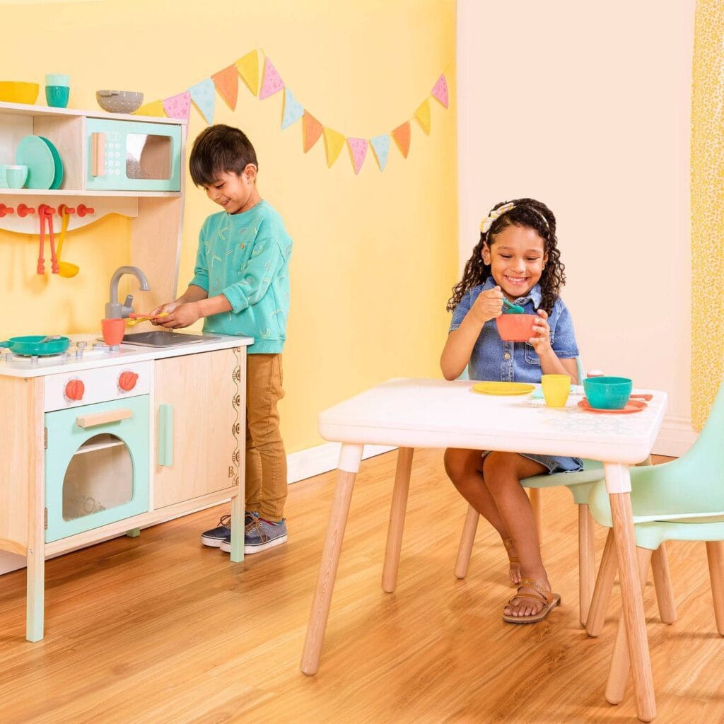 Kids playing in a colorful yellow and pink room with a wooden play kitchen.