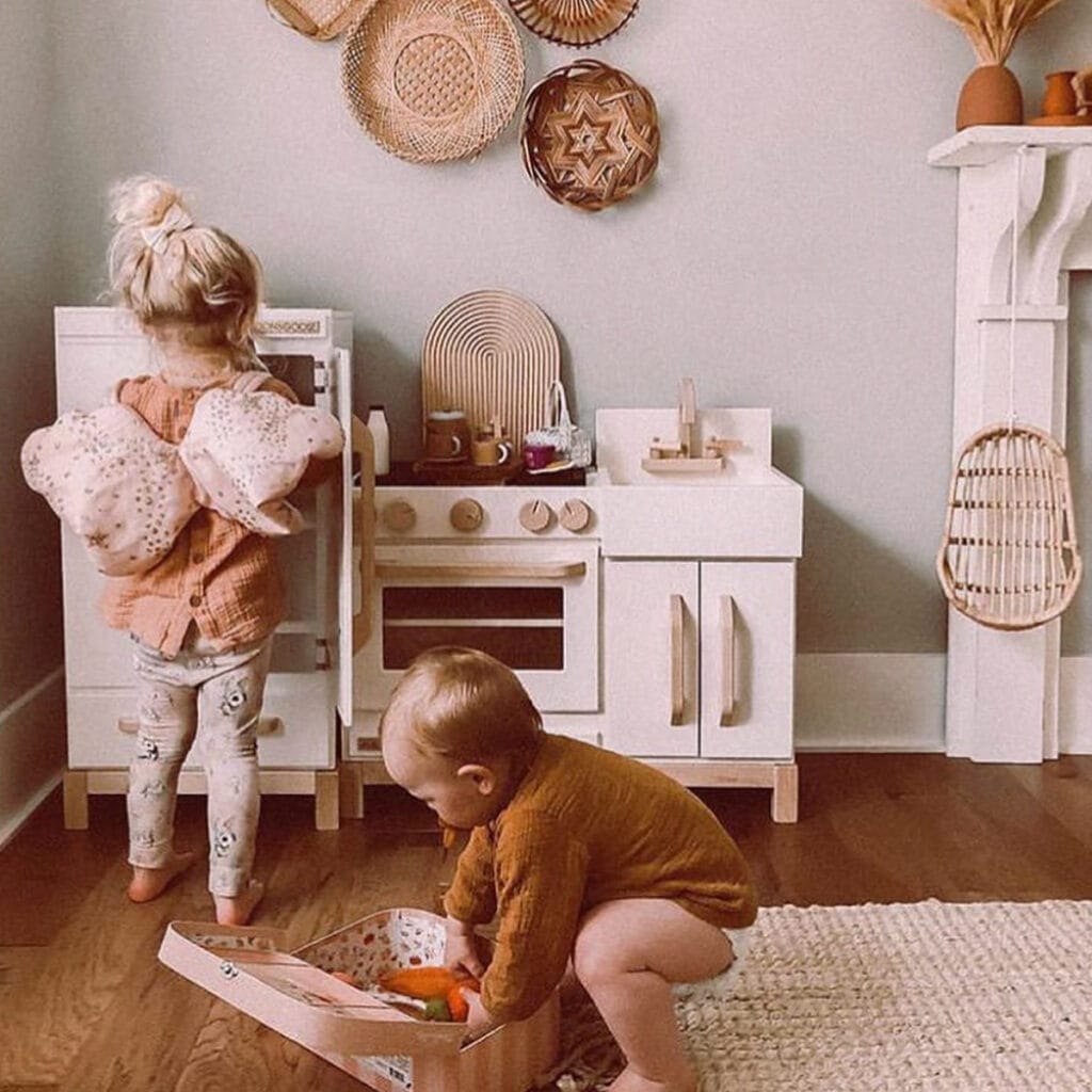 little kids playing with a white and wood kithcen with natural wood and white accents in the room.