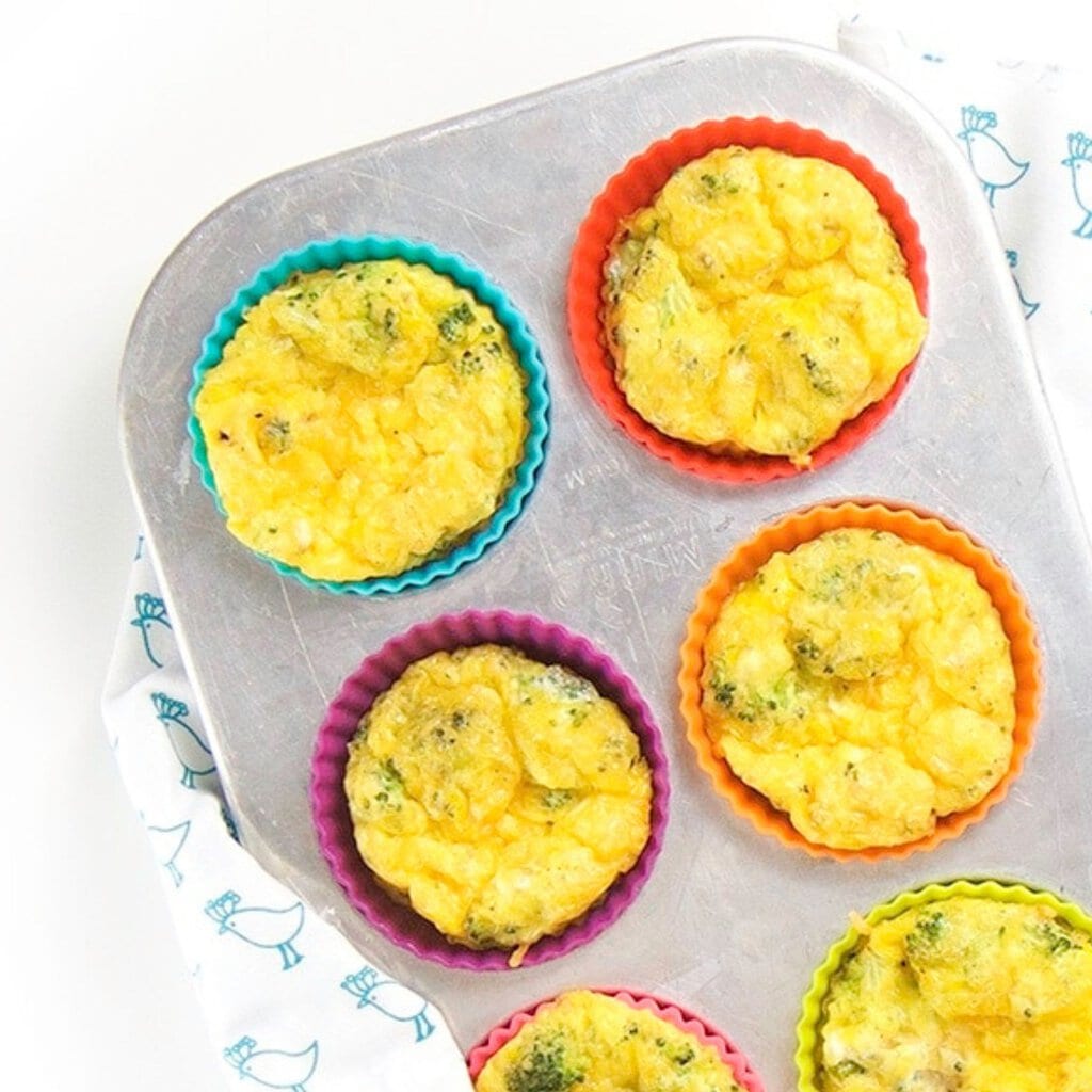 Silver muffin tray with colored muffin liners with egg cups inside with a white and blue patterned napkin sitting on my white countertop. 