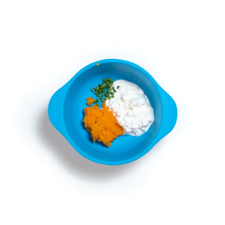 A blue baby bowl filled with mashed steamed carrots cottage cheese and chives.