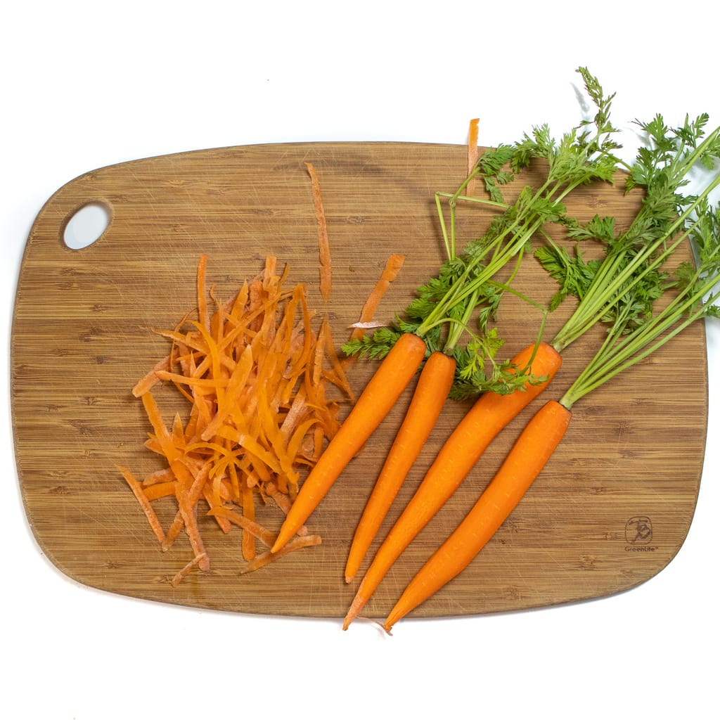 A wooden cutting board on a white background with peeled carrots sitting on it.