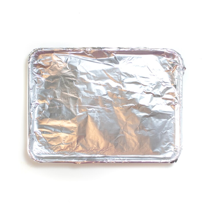 A silver baking sheet with carrots with tinfoil on top.