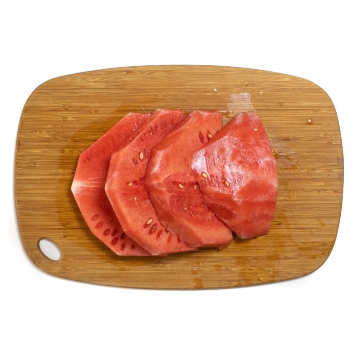 Four slices of watermelon sitting on a white wooden cutting board