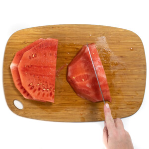 A pair of hands with a knife cutting each slice of watermelon into slices