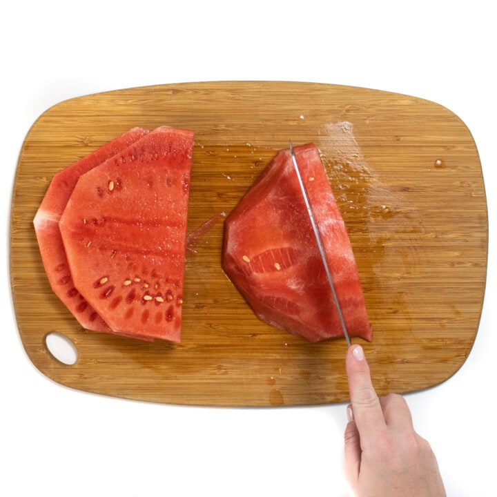A pair of hands with a knife cutting each slice of watermelon into slices
