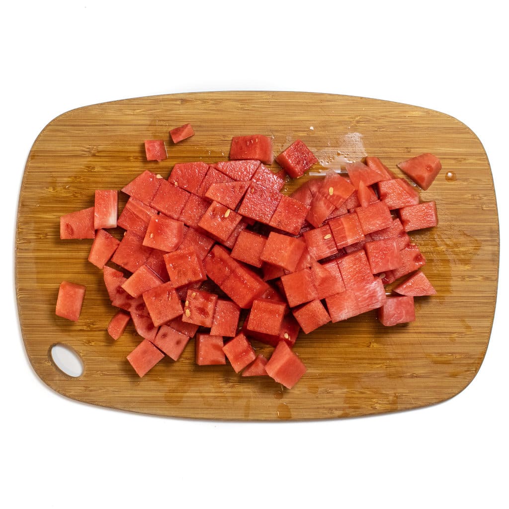 A wooden cutting board full of cubes of watermelon