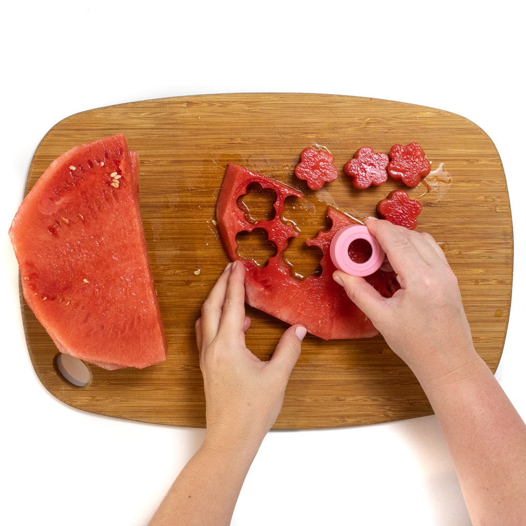 A slice of watermelon being cut into flower shapes with a cookie cutter.