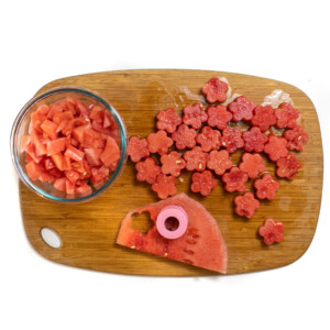A slice of watermelon being cut into flower shapes with a cookie cutter.