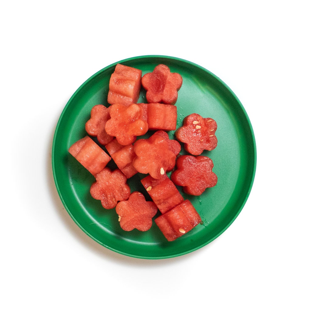 A green plate with flower shaped pieces of watermelon.
