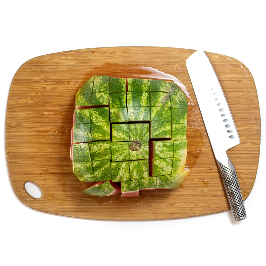 A watermelon on the cutting board cut into long strips with the rind showing.