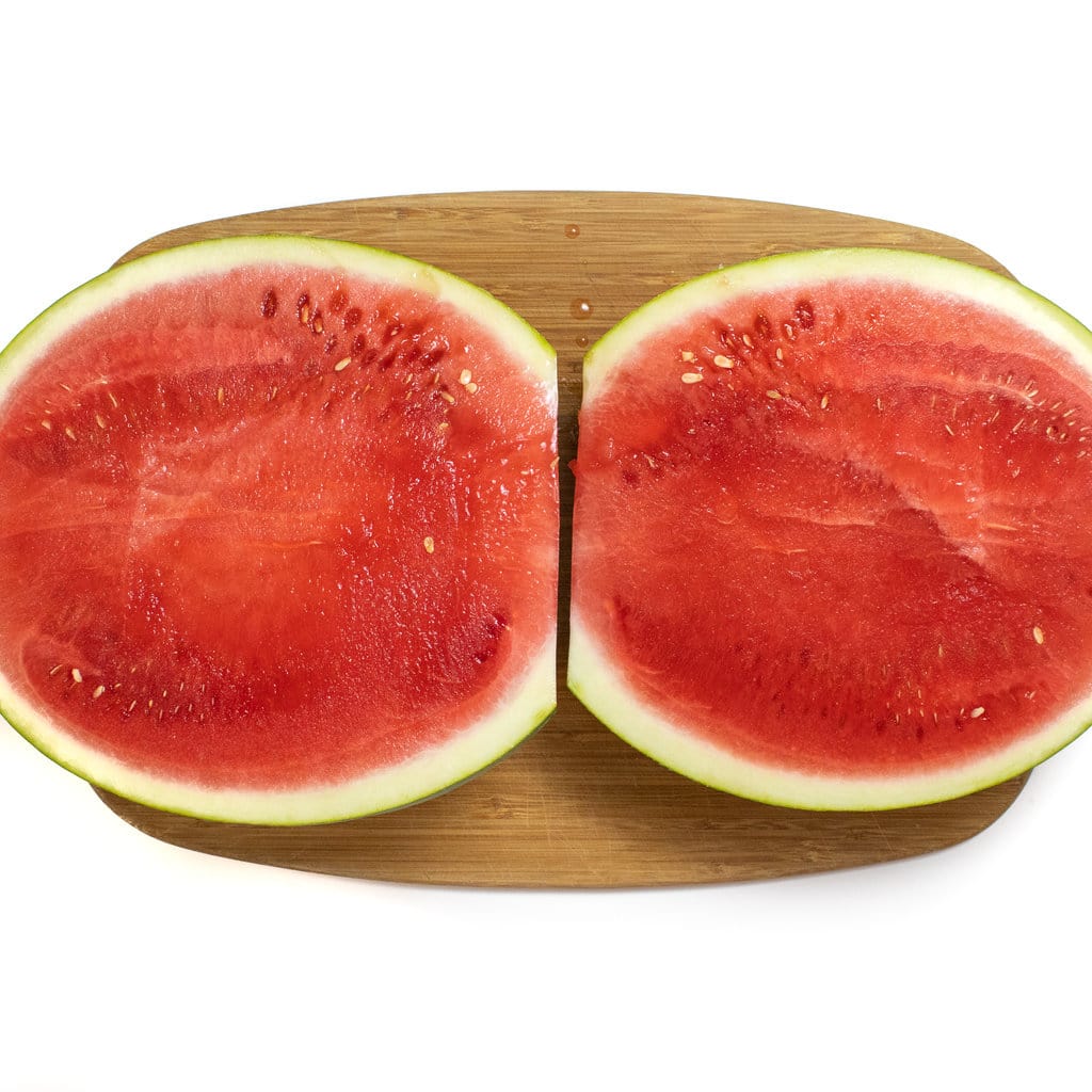 A watermelon cut in half and the two halves open on a wooden cutting board.