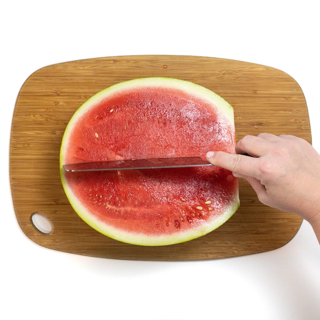 What are melon on a cutting board with a hand holding a knife cutting it in half.