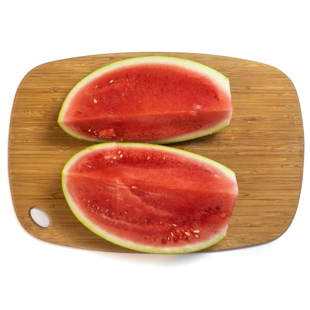 Two wedges of a watermelon on a wooden cutting board against a white background.