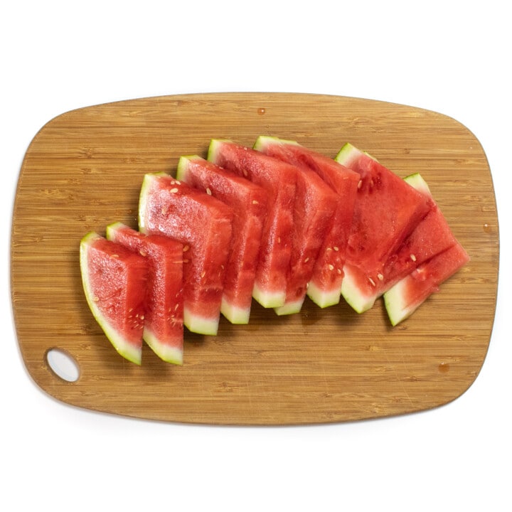 A wooden cutting board with a fan of sliced watermelon on it.
