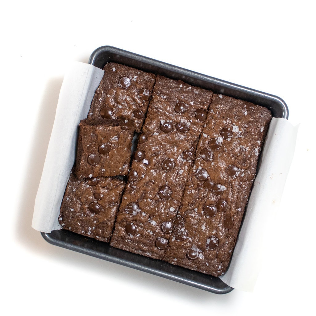 A pan of brownies halfway cut into squares against a white background.