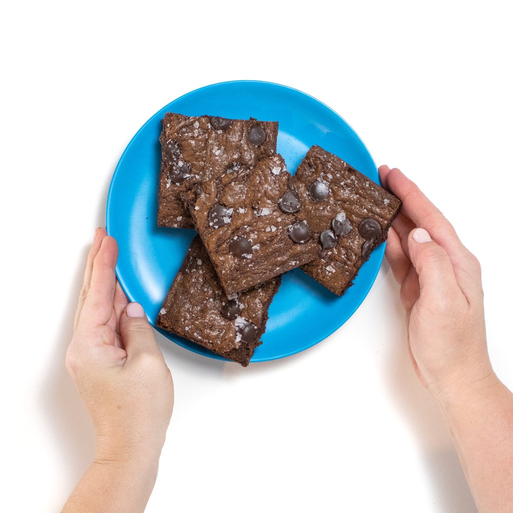 Hands holding a blue plate with foursquare brownies on it.