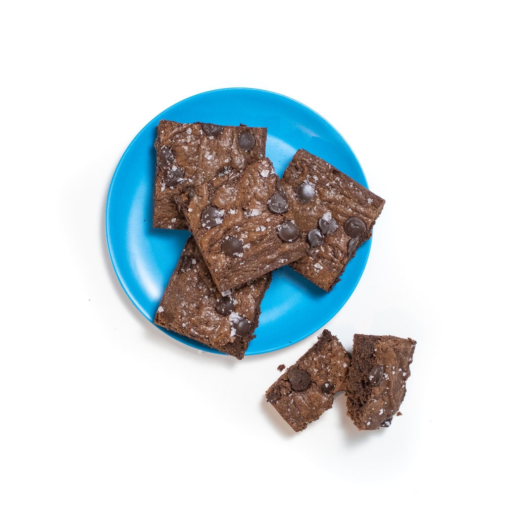 A blue plate with four brownies and a fifth brownie cut in half sitting off to the side against the white backdrop.
