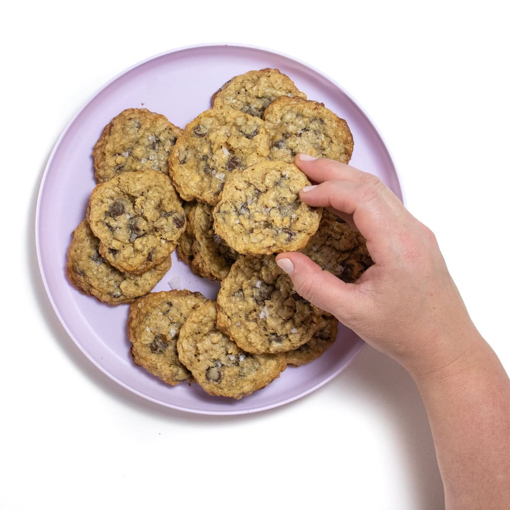 A purple plate full of chocolate chip oatmeal cookies for lactation with a hand holding a cookie up.