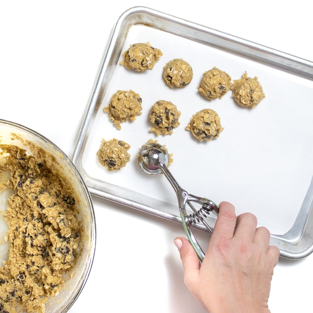 A hand using a cookie scoop to place a cookie scoops on a baking sheet ready for the freezer.