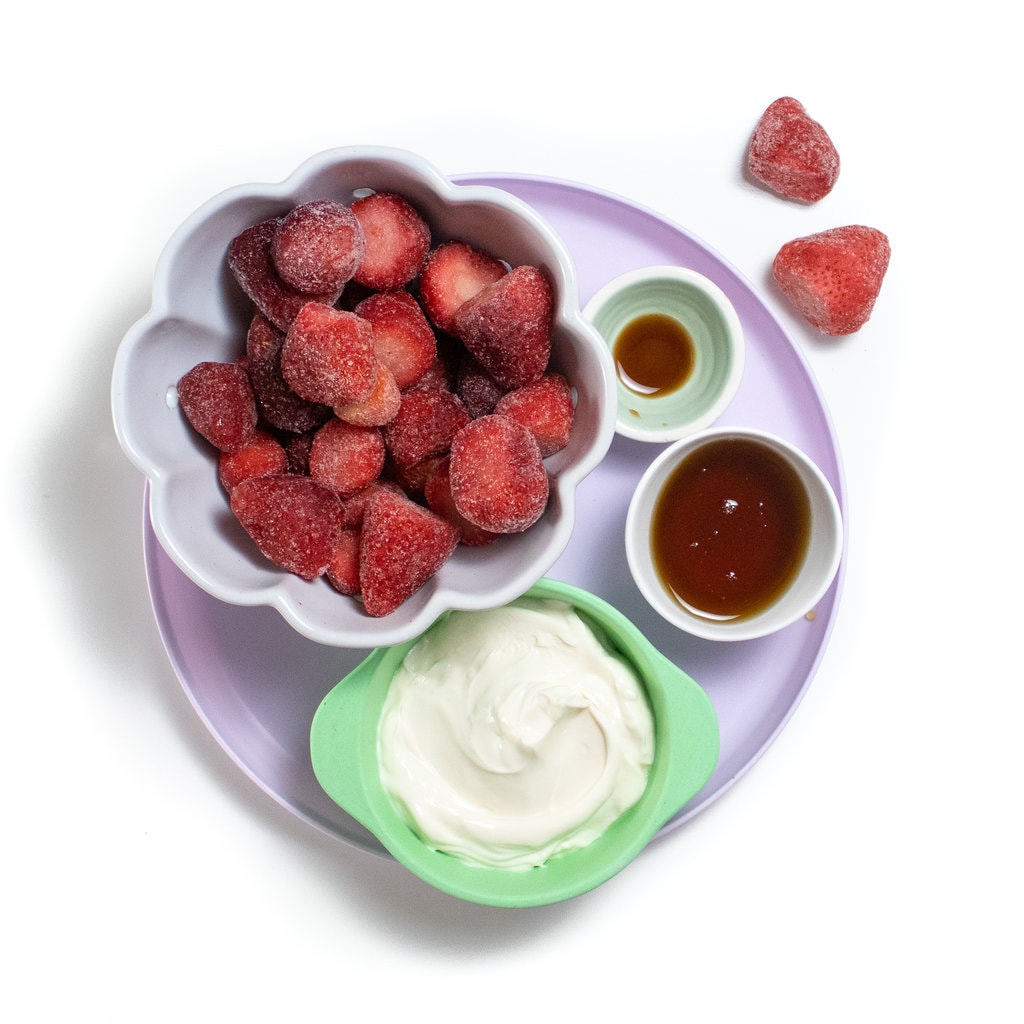 Ingredients for strawberry yogurt popsicles on a purple plate.
