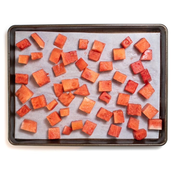 A baking sheet with cubes of watermelon on a parchment paper