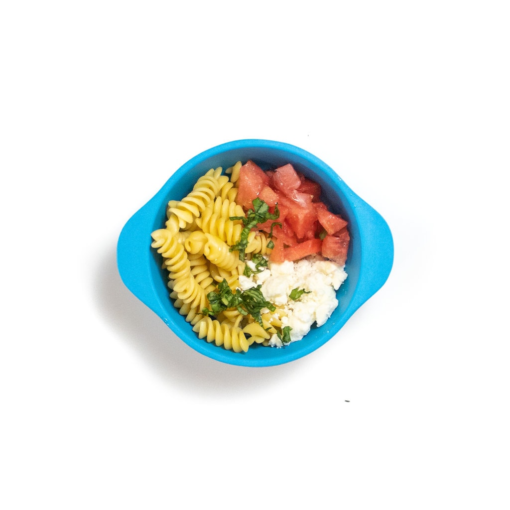 A blue baby bowl filled with pasta, basil, feta and watermelon.