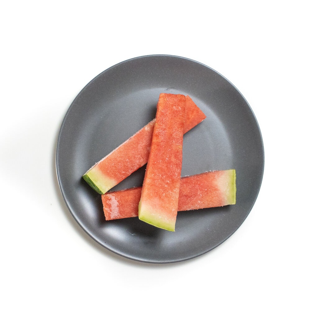 A gray baby plate with three sticks of frozen watermelon.