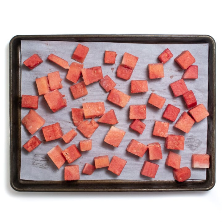 A baking sheet with cubes of watermelon frozen.