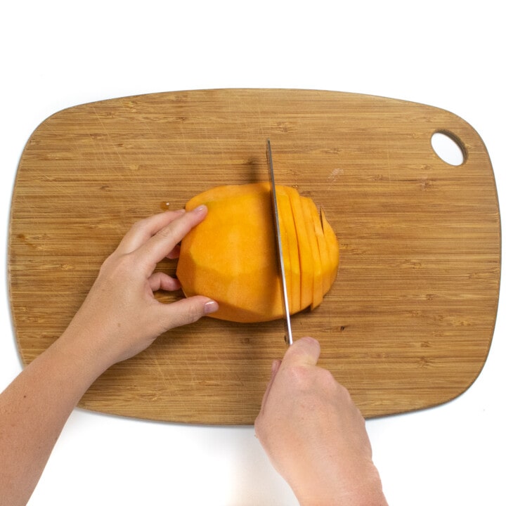 Half of a cantaloupe being sliced into small slices.