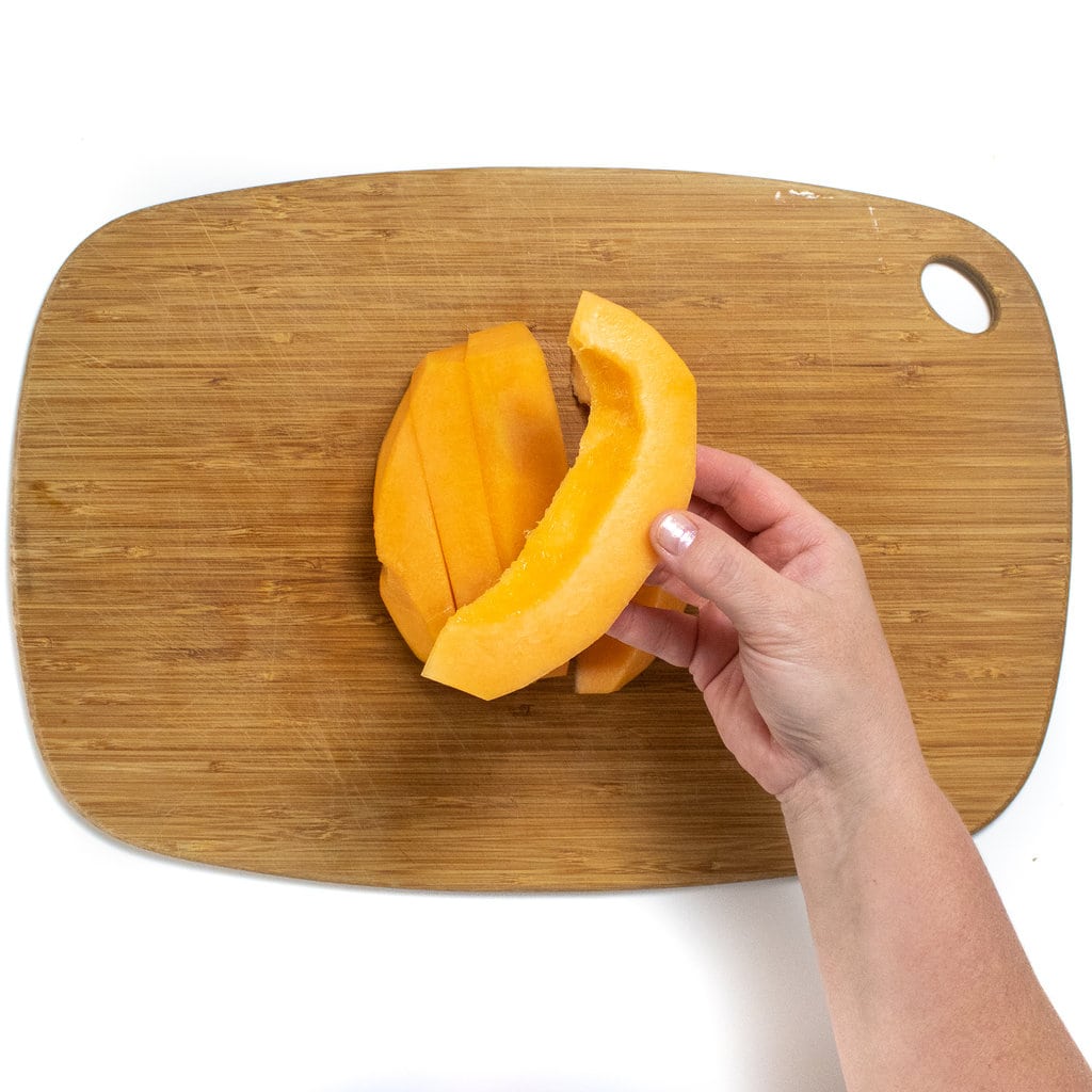 Hands holding a wedge of Cantelope over a wooden cutting board.