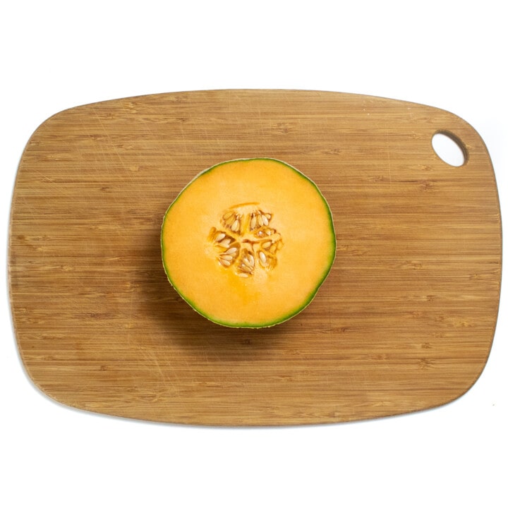 Half of a cantaloupe sitting on a wooden cutting board.