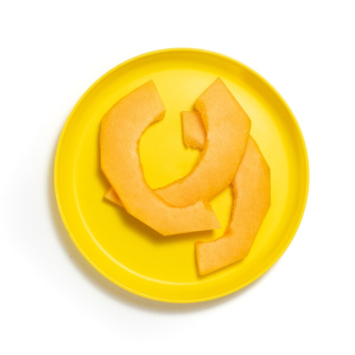 A yellow kids plate with three slices of cantaloupe against a white background.