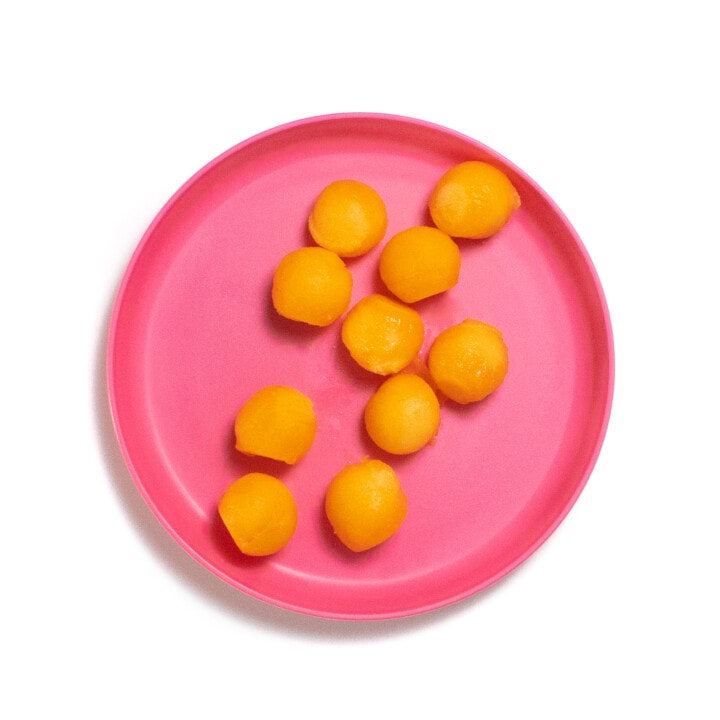 A pink kids plate with cantaloupe balls against a white background