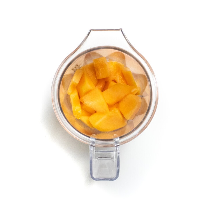 A clear blender with chunks of cantaloupe against a white background.